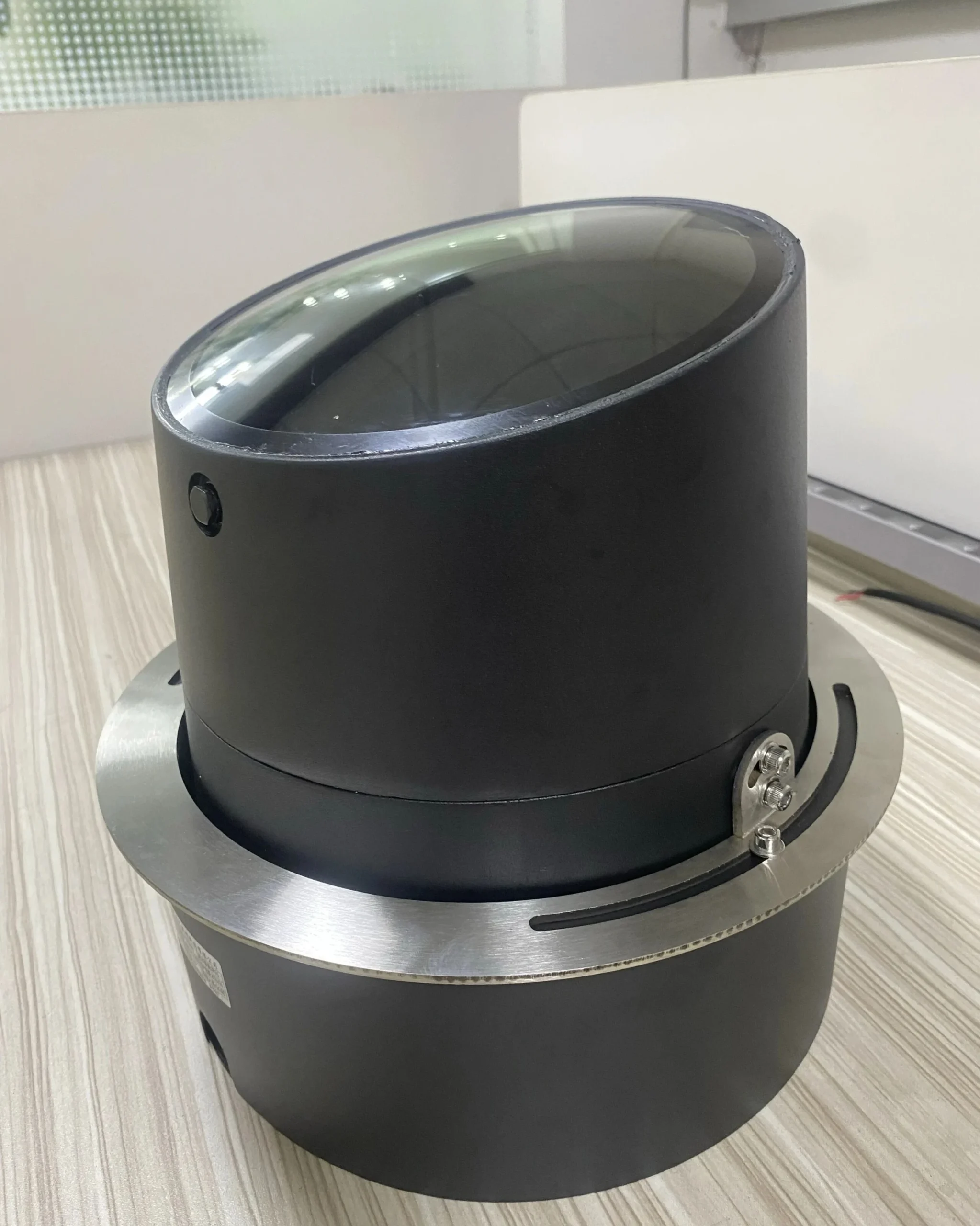 Holofote LED semienterrado com corpo cilíndrico inclinado e aro de acabamento em aço inoxidável, visto de frente